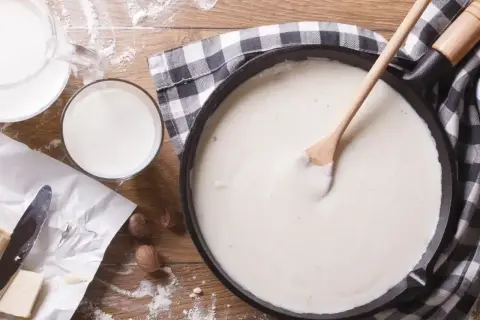 Gładki sos beszamel w patelni, obok mleko, masło i mąka.