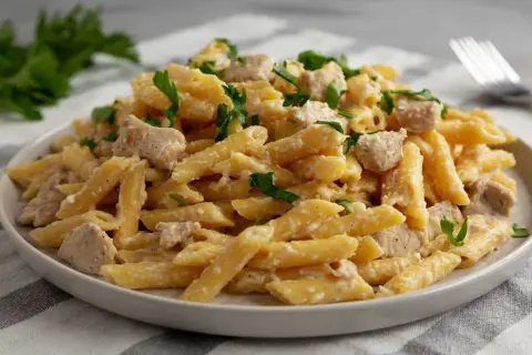 Penne w kremowym sosie ze smakowitymi kawałkami kurczaka, posypane świeżą natką pietruszki. Idealne danie na szybki obiad.