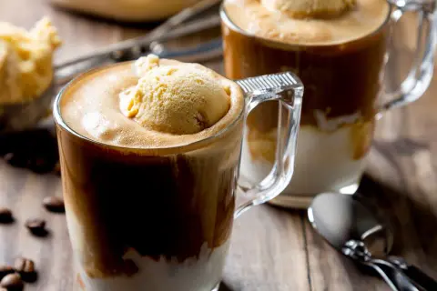 Dwa kubki affogato z lodami waniliowymi i kawą, na drewnianym stole z ziarnami kawy.