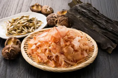 Suszone rybki, grzyby shiitake, płatki bonito i wodorosty kombu na drewnianym tle.