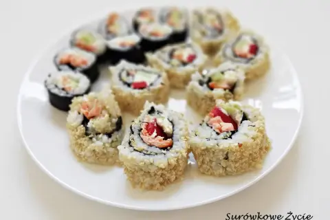 Talerz z rolkami sushi uramaki, niektóre obtoczone w sezamie, z widocznym łososiem i warzywami.