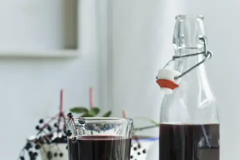 Szklanka i butelka z ciemnym sokiem z czarnego bzu, ozdobione gałązkami z owocami.