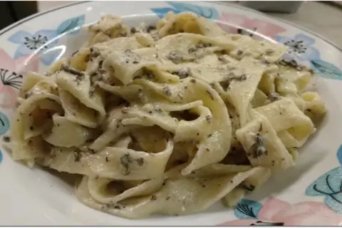 Pappardelle z kremowym sosem, w którym wyczuwalne są kawałki trufli. Makaron z pastą truflową i śmietaną wygląda apetycznie.