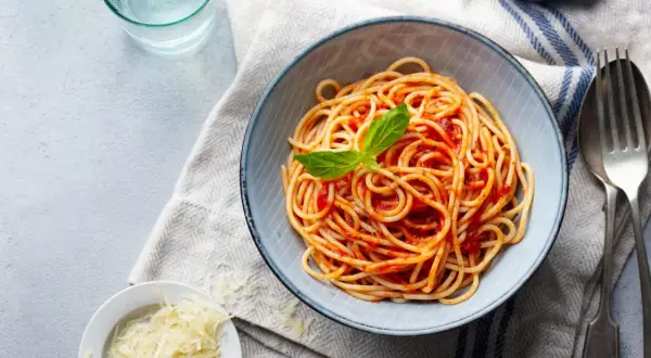 Misternie ułożone spaghetti z sosem pomidorowym i listkiem bazylii. Obok miseczka z tartym parmezanem. Idealne pytanie: jakie przyprawy do spaghetti?