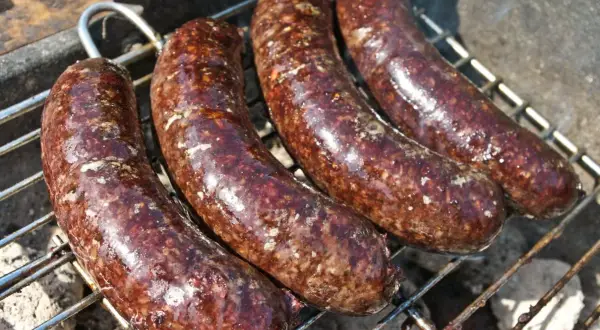 Cztery soczyste kaszanki z grilla pieką się na ruszcie, uwalniając apetyczny aromat.