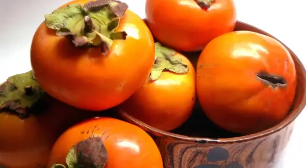 Kilka pomarańczowych owoców persymony (kaki) w drewnianej misce.