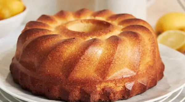 Puszysta babka z wgłębieniem pośrodku, na talerzu, z cytrynami w tle.