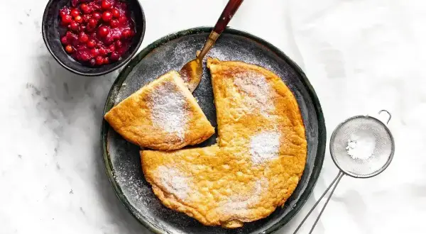 Puszysty omlet posypany cukrem pudrem, podany z żurawiną i łyżką.