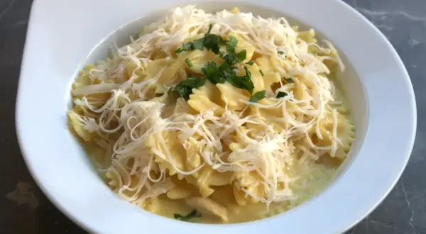 Szybki obiad z twarogiem: makaron farfalle w kremowym sosie, posypany startym serem i natką pietruszki.