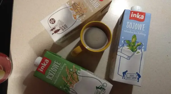 Trzy kartony napojów Inka (owsiane, sojowe, ryżowe) i kubek kawy.
