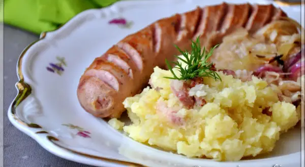 Biała kiełbasa z ziemniakami i kapustą kiszoną, udekorowana koperkiem.