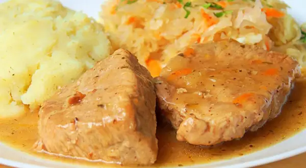 Soczysta szynka wieprzowa w sosie, podana z puree ziemniaczanym i surówką z kiszonej kapusty. Idealny pomysł, jak zrobić szynkę wieprzową na obiad.