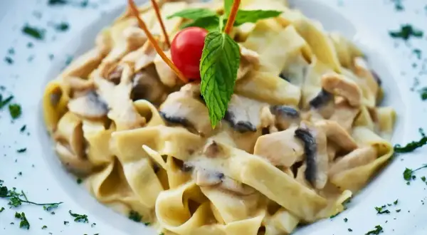 Tagliatelle z kurczakiem i grzybami w sosie śmietanowym, udekorowane pomidorkiem i miętą.