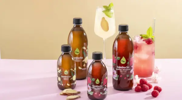 Butelki z kombuchą, drinki, maliny i imbir na różowym tle.