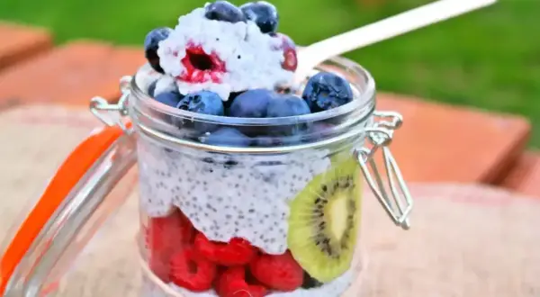 Pudding chia z owocami w słoiku: maliny, borówki, kiwi i łyżka z deserem.