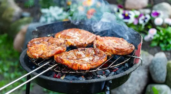 Soczysty karczek na grillu, idealny przykład, jak zamarynować karczek na grilla. Dym unosi się nad grillowanymi mięsami.