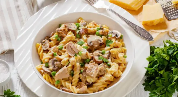 Makaron fusilli z tuńczykiem, groszkiem i pieczarkami w kremowym sosie, udekorowany natką pietruszki.