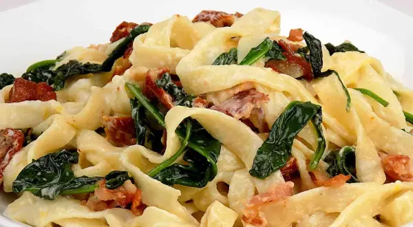 Makaron tagliatelle z kremowym sosem, szpinakiem i kawałkami boczku.