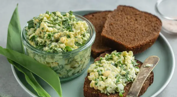 Jajeczna pasta z czosnkiem niedźwiedzim w słoiku i na kromce chleba.