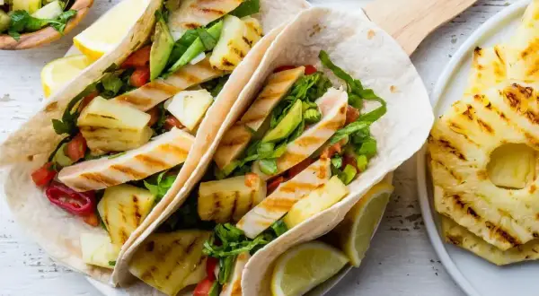 Tacos z grillowanym kurczakiem, ananasem i warzywami, podane z cytryną.