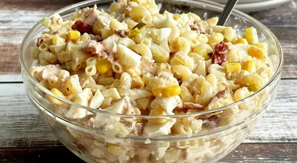 Szklana miska pełna sałatki makaronowej z tuńczykiem, jajkiem i kukurydzą.