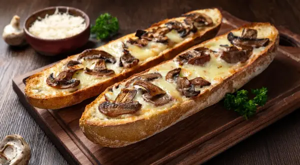 Dwie zapiekanki z bagietki z pieczarkami i serem na drewnianej desce.