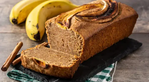 Wilgotny chlebek bananowy z plasterkami banana na wierzchu, obok banany i laski cynamonu.