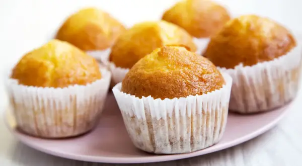 Kilka złotych muffinek w papierowych foremkach na różowym talerzu.