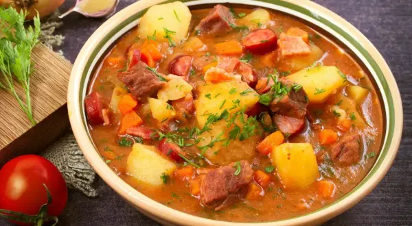 Gęsty gulasz z ziemniakami, mięsem i kiełbasą, posypany natką. Idealny obiad na dwa dni, sycący i aromatyczny.