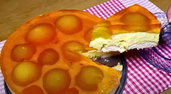 Sernik na zimno z brzoskwiniami w galaretce, z wyciętym kawałkiem.