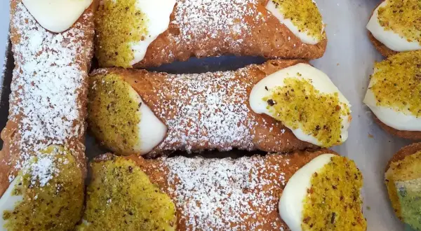 Sycylijskie cannoli z kremem i pistacjami, posypane cukrem pudrem.