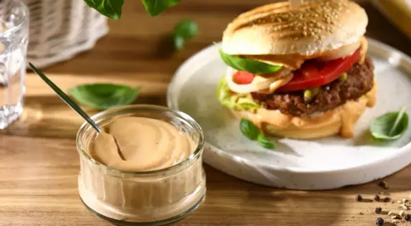Domowy sos do burgerów w słoiczku obok gotowego burgera na talerzu.