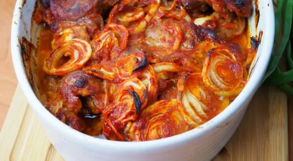 Pieczona karkówka z cebulą w sosie pomidorowym w naczyniu żaroodpornym.