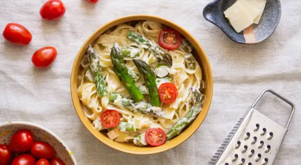 Makaron tagliatelle ze szparagami i pomidorkami koktajlowymi w sosie śmietanowym.