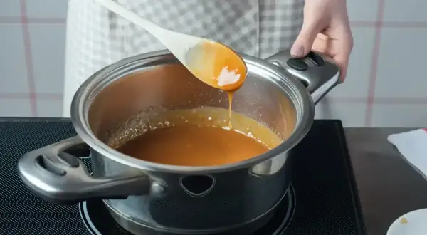 Gotowanie domowego kajmaku w garnku, gładka, karmelowa masa spływa z drewnianej łyżki.