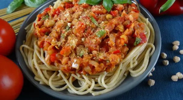 Talerz spaghetti z sosem z ciecierzycy, pomidorami, papryką i bazylią.