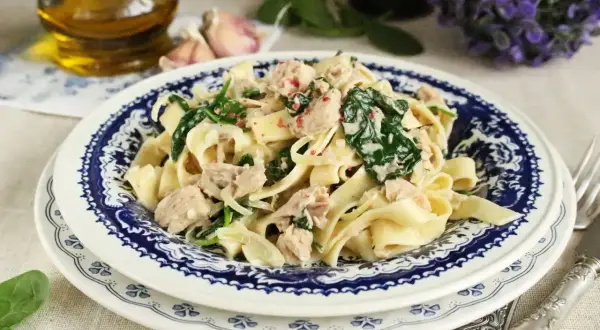 Makaron tagliatelle z tuńczykiem i szpinakiem w kremowym sosie, podany na talerzu z niebieskim wzorem.
