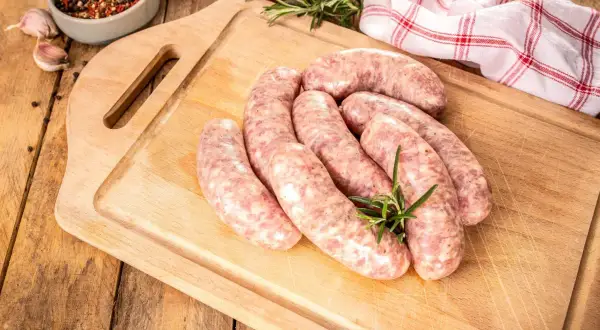 Surowe kiełbaski na desce, obok przyprawy i czosnku. Zastanawiasz się, jak długo parzyć kiełbasę, by była idealna?