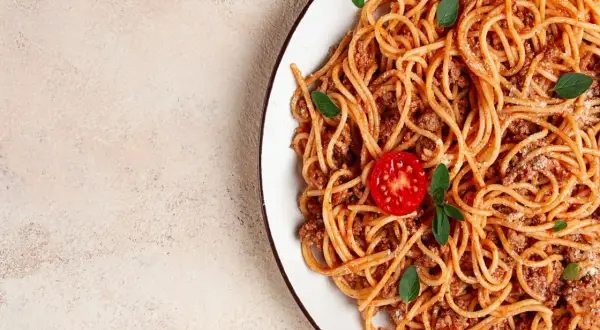 Talerz spaghetti bolognese z pomidorkiem i bazylią. Idealne dodatki do spaghetti, które zachwycą każdego smakosza.