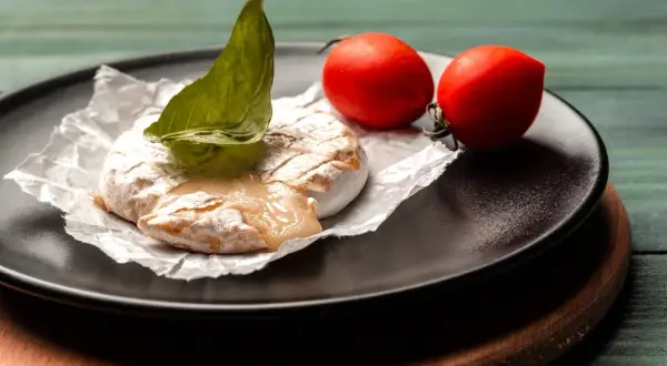 Grillowany ser camembert z pomidorkami koktajlowymi i bazylią na talerzu.