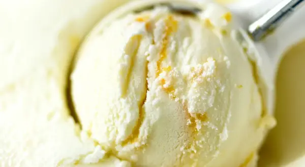 Łyżka do lodów nakłada kremowe lody waniliowe z pomarańczowymi smugami.