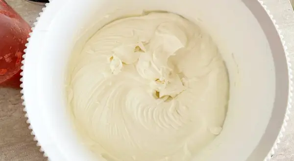 Krem z mascarpone w białej misie, obok miseczka z truskawkami.