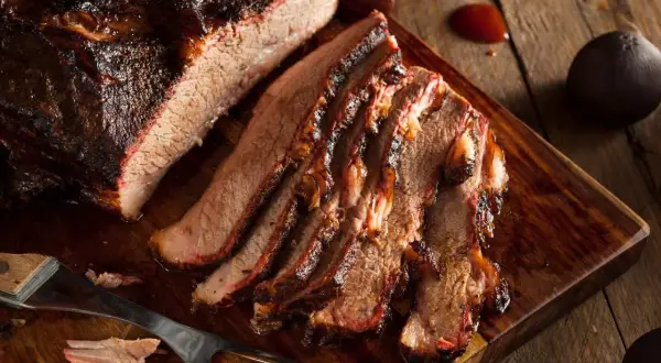 Pokrojona wołowina brisket z ciemną skórką, ułożona na drewnianej desce.