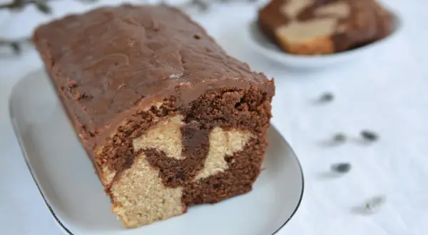 Wilgotna babka marmurkowa z czekoladową polewą na białym talerzyku.