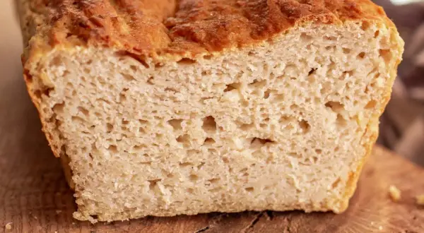 Przekrojony bochenek chleba bezglutenowego na drewnianej desce, z widocznym puszystym wnętrzem.