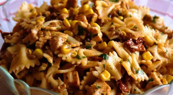 Sałatka z makaronem farfalle, kurczakiem, kukurydzą i suszonymi pomidorami w szklanej misie.