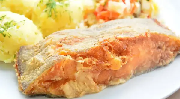 Smażony filet z ryby z ziemniakami i surówką na talerzu.