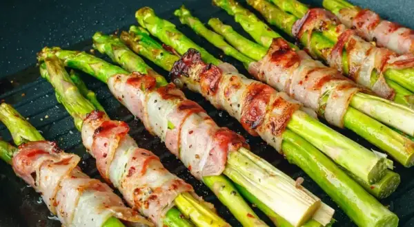 Grillowane szparagi owinięte boczkiem na patelni grillowej.