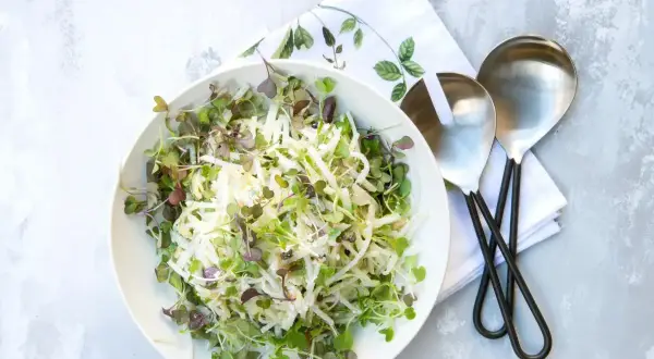 Sałatka coleslaw z kiełkami w białej misce, obok serwetka i łyżki do sałatek.