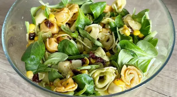 Sałatka z tortellini, kukurydzą, suszonymi pomidorami i zieloną sałatą w szklanej misce.